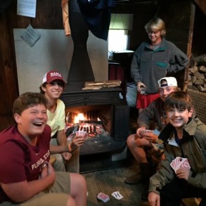 Some of the crew enjoys cards around the stove while the rain falls outside.